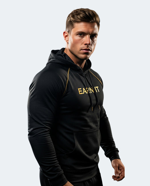 A muscular man wearing a black long-sleeve athletic hoodie with gold 'EARN IT' text on the chest, posed against a light gray background.